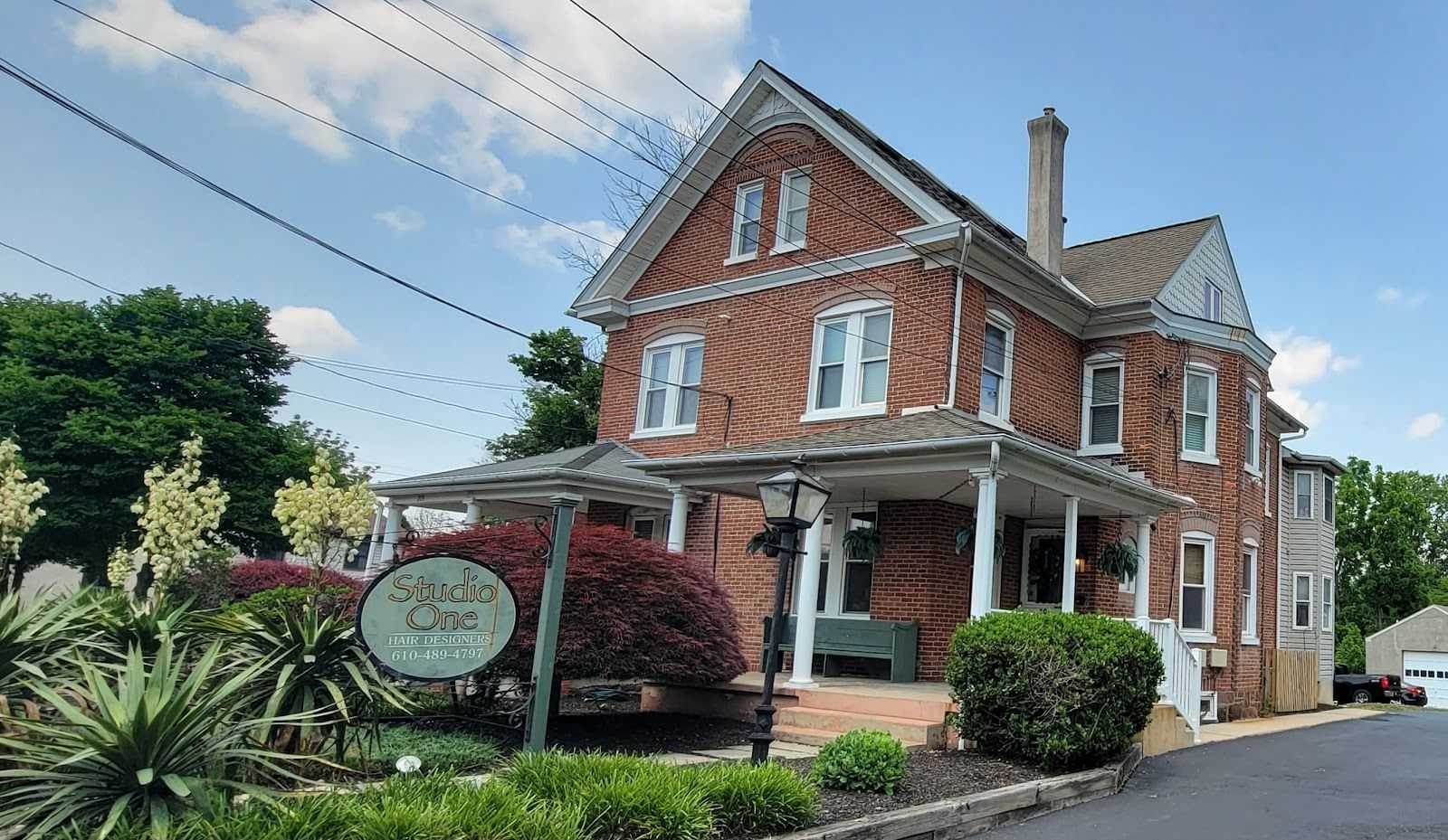 Red-brick house with Studio One Photography sign, surrounded by greenery.